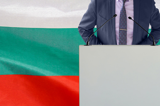 Tribune with microphone and man in suit on Bulgaria flag background. Businessman and tribune on Bulgaria flag background. Politician at the podium with microphones background Bulgaria flag. Conference