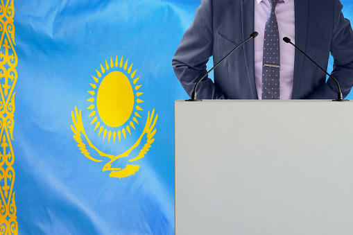 Tribune with microphone and man in suit on Kazakhstan flag background. Businessman and tribune on Kazakhstan flag background. Politician at the podium with microphones background Kazakhstan flag