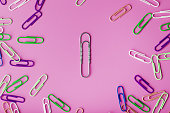 A large paper clip surrounded by small colored paper clips on a pink background