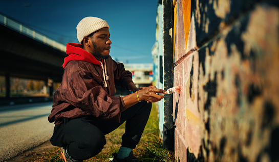 Closeup side view of a young African American man creating street art drawing on the wall.