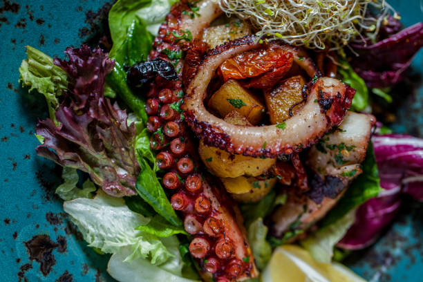 istock Fried octopus with salad, fried potatoes, microgreen in a blue ceramic plate. Wooden background with a painting, a ceramic vase and a glass of white wine. 1445222545