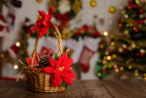 Wicker basket decorated with poinsettia on wooden table and Christmas background.