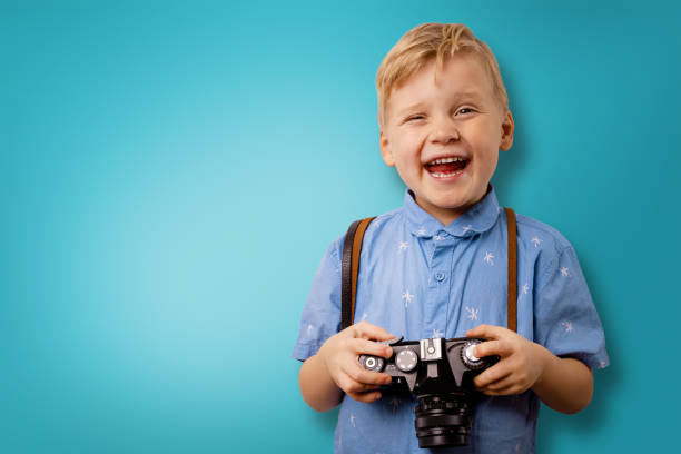 happy little boy with retro camera on blue background with copy space. photography courses