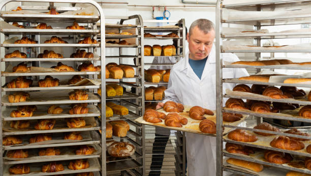 istock Worker of bakery putting baked baguettes on tray rack 1445231077