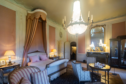 UTRECHT, NETHERLANDS - AUGUST 09, 2022: Luxurious bedroom of Baroness Rothschild in De Haar Castle with wide bed with canopy, carved furniture, crystal chandelier and family photos on bedside tables