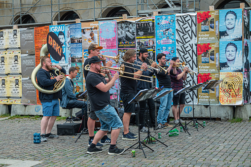 Copenhagen, Denmark - July 23, 2022: DRS! brass band in action on Højbro Plads, square. All males in front of colorful commercial poster wall