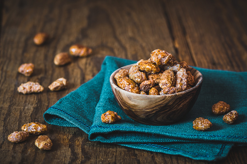Bowl of sweet candied almonds on rustic wooden background
