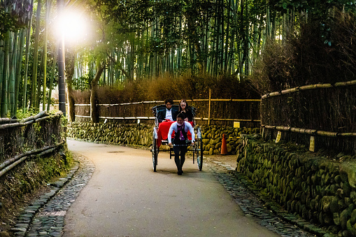 Kyoto, Japan - October 17, 2022: Rickshaw carrying a couple through arashiyama bamboo forest tourist park attraction in Kyoto Japan