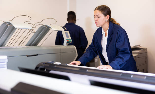 istock Concentrated young female typographer in a blue robe uniform pressing the buttons on the plotter in the typography 1445233232