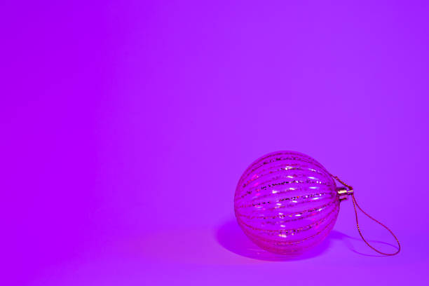 Close-up of a shiny glass Christmas ball on an old wooden table and a blurred glittering background with a copy of the space.