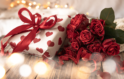 Composition for Valentine's Day with a gift box and a bouquet of roses on a blurred background with bokeh lights.