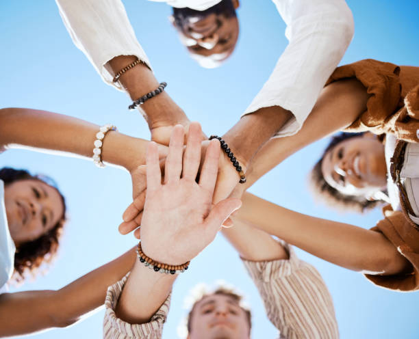 istock Friends, trust and support hands low angle for solidarity in multicultural group with blue sky. Care, respect and love in friendship with young people who enjoy happy emotional bond together. 1445243469