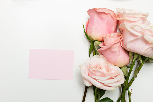 Pink paper  and pink roses on white table. Romantic Greeting Card template