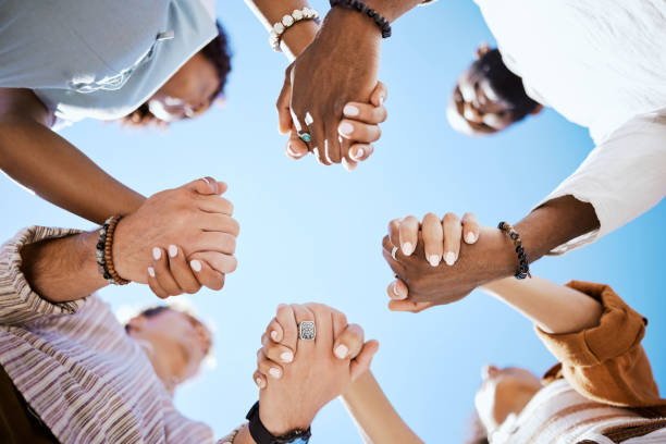 Diversity, support and people holding hands in trust and unity for community against sky background. Hand of diverse group in solidarity for united team building collaboration and teamwork success stock photo