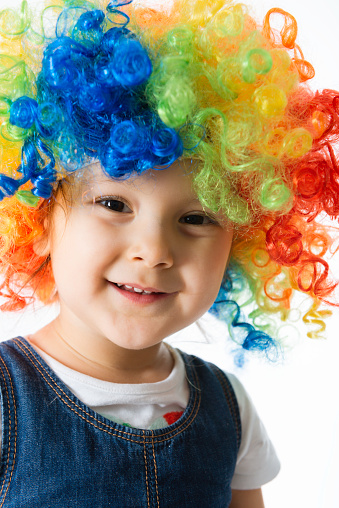 Cute little girl with clown wig is laughing and looking at camera in front of white background.