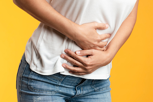 Unrecognizable female is holding her belly with her two hands because of abdominal pain.