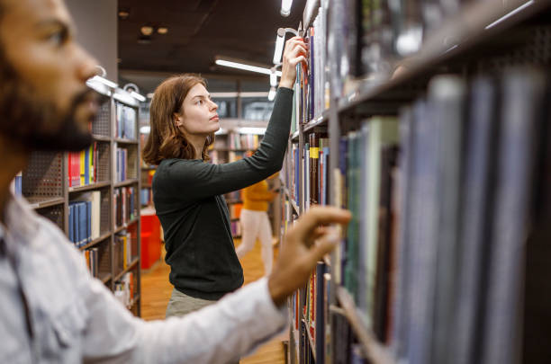 Two people searching for books in the library stock photo