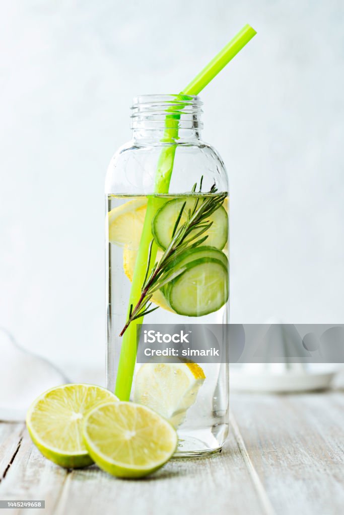 Detox Bottle of infused water on white wood with a slice of lemon , cucumber and rosemary leaf in it. Infused Water Stock Photo
