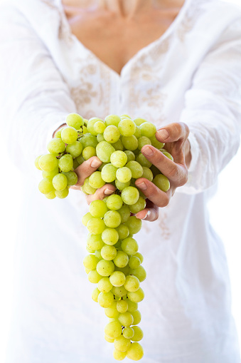 Caucasian woman is holding a bunch of grapes in hand.