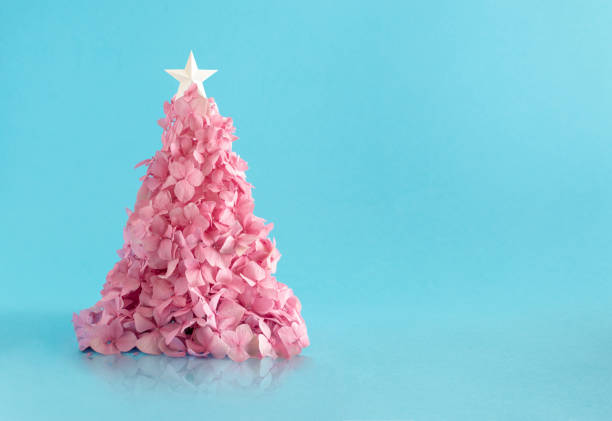 Christmas tree made of a small pink flowerers against light blue background. Minimal flat lay composition.