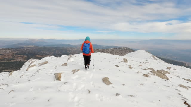 Successful female mountain climber is walking on the ridge of the snowy mountain summit in winter