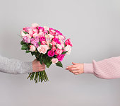 Hand giving roses flowers bouquet to woman on grey background. Valentines or mothers day concept.