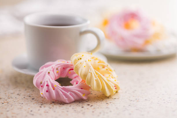 Different colors meringues with sprinkles and tea cup on kitchen table.