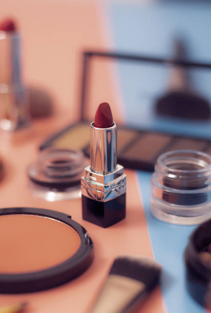 One red lipstick on a pink-blue background with a blurry set of female cosmetics, close-up side view with depth of field. The concept of cosmetics, beauty salon.