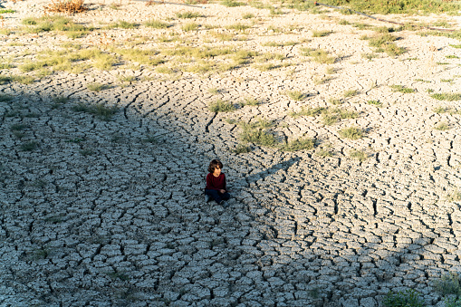 boy sitting on desert land. cracks have formed in the dehydrated soil. Taken from a high angle with a full frame camera.