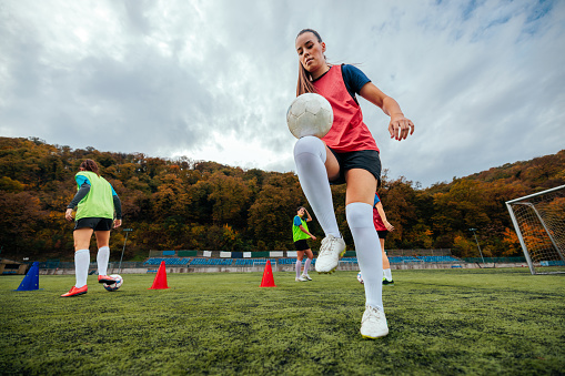 A skillful female football player is on the field  practicing by balancing the ball on her knee.