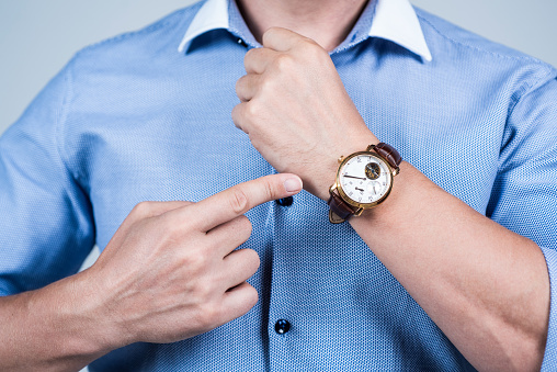 Mature man talking on the phone and checking the time on his wristwatch at office