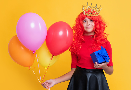 glad child in crown with gift box and party balloon on yellow background.