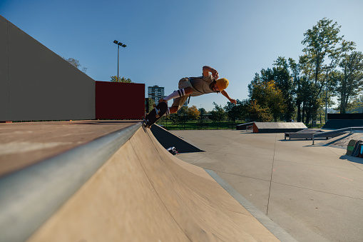A young Caucasian skater is having fun in the skatepark riding his skateboard on the ramps.