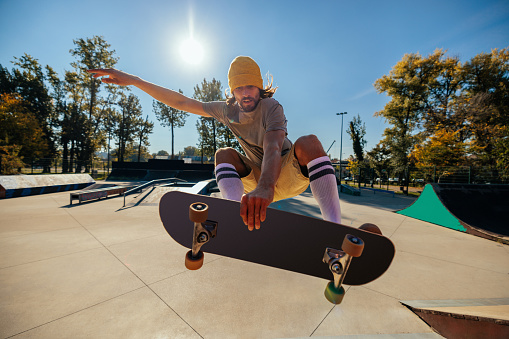 A Caucasian skater is in the skatepark jumping with his board in the air.