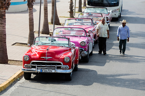 Havana, Cuba - April 9, 2018: Street scene with a vintage American cars in Old Havana (La Habana Vieja), two drivers walking on the street, Cuba.