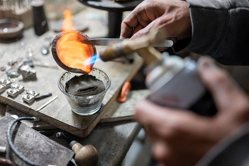 A craftsman jeweler is pouring some melted silver in a mold to make an unique piece. Concept of craft work