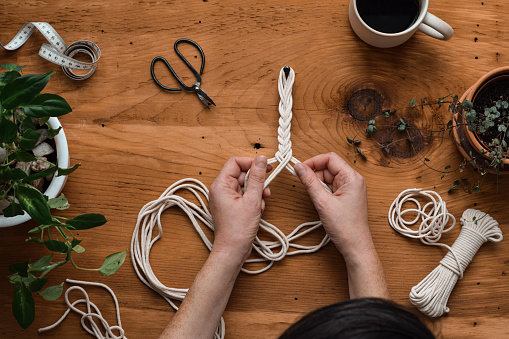 Top down view of woman's hands making macrame plant hanger
