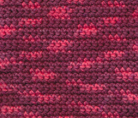 Fabric crocheted with red and pink cotton yarn, close-up background.
