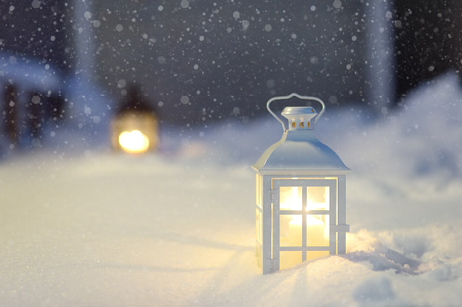 Large lantern with burning candle on street of small town during snowfall on Christmas eve. Stylish Xmas decorations among snowdrift. Festive street decor in New Year holiday. Winter holiday tradition