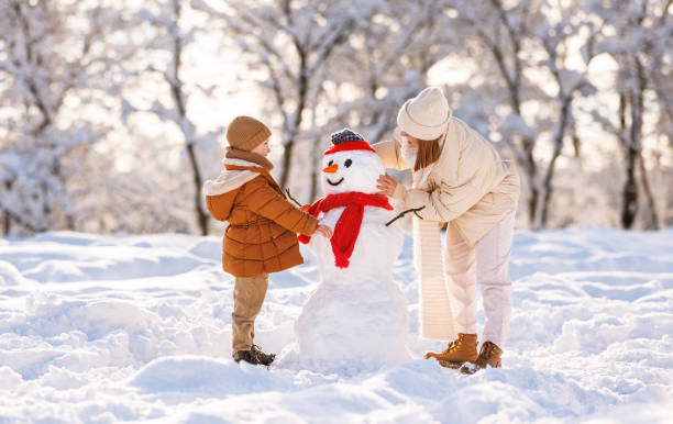 istock Cute little boy making snowman with mom in winter park 1445277132