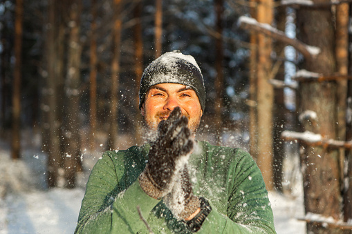 Attractive man in the winter forest plays snowballs. Wimter lifestyle concept.