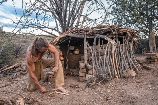 Man making friction fire in front of shelter stock photo