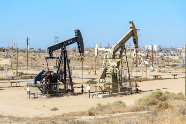 pumpjacks en un campo petrolero bajo el cielo azul - pozo de petróleo fotografías e imágenes de stock