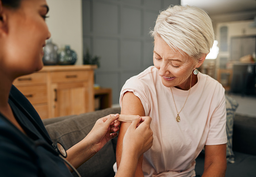 Covid vaccine, plaster and doctor with patient in a health consultation at a retirement house. Nurse, healthcare worker and elderly woman with a bandaid on her arm after a treatment in a nursing home