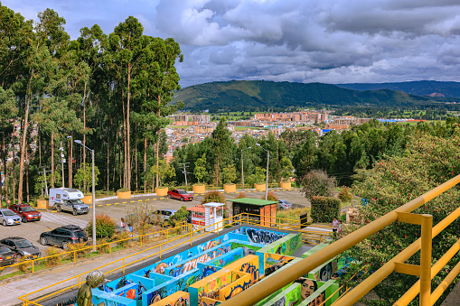 Zipaquirá, Colombia - October 28, 2022: A view of a section of the public car park and beyond to a section of the City, from just outside the Salt Cathedral, or Catedral de Sal, as it is called in Spanish. In the foreground, is a maze for children to play in. The city is located on the Eastern Range of the Andes Mountains, at an altitude of 8,690 feet above mean sea level. Far background: Andes Mountains. Photo shot in the afternoon sunlight on an overcast day; horizontal format.