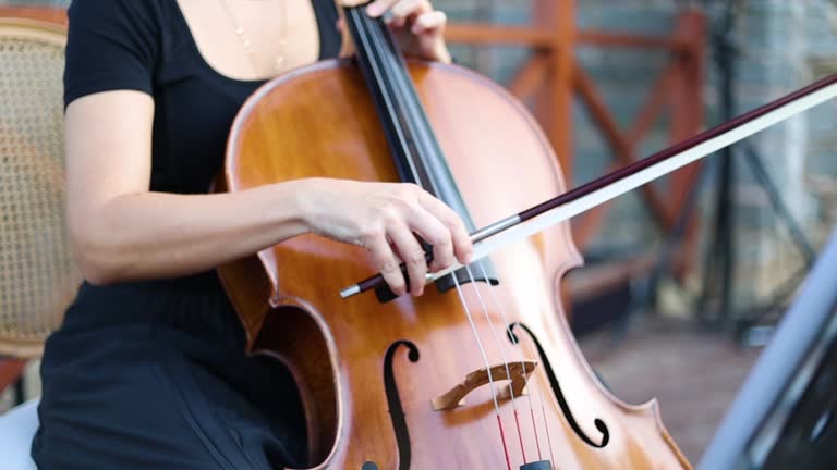 Female cellist working with her instrument, woman playing cello outside, beautiful female cellist,Woman's hand playing a cello,Woman cellist's hands adjust the brown cello and control it with bow,Concept of tuning musical instrument