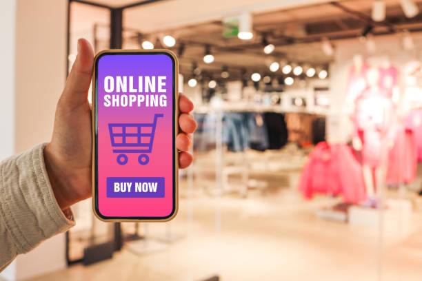 Online shopping. Phone in hand with the application of the site buy online against the background of a clothing store stock photo