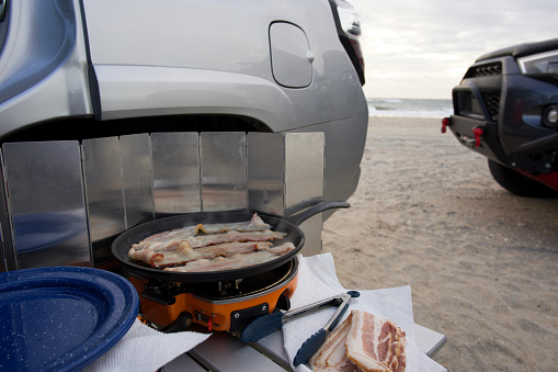 Cooking bacon on camping stove in ocean beach campsite while overlanding