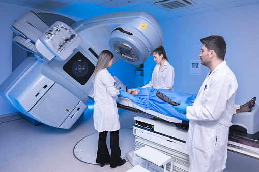 A young woman is undergoing radiation therapy for cancer under the supervision of doctors in a modern cancer hospital. Cancer therapy, advanced medical linear accelerator.