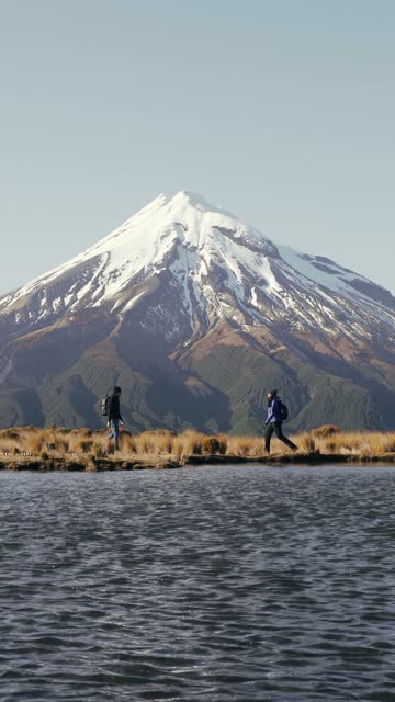 Young couple of backpackers embracing each other by lagoon with amazing view of snowy peak mountain